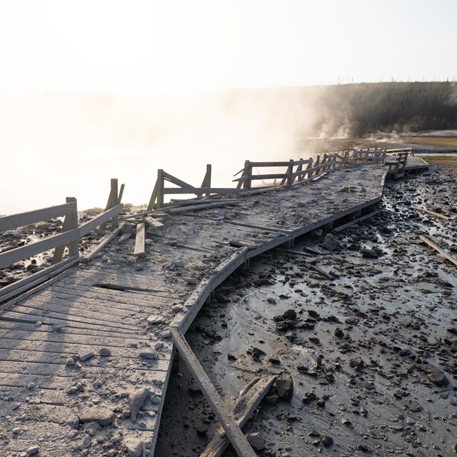 a damaged wooden boardwalk covered in rock and debris