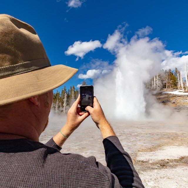 A person photographing the an eruption of a geyser