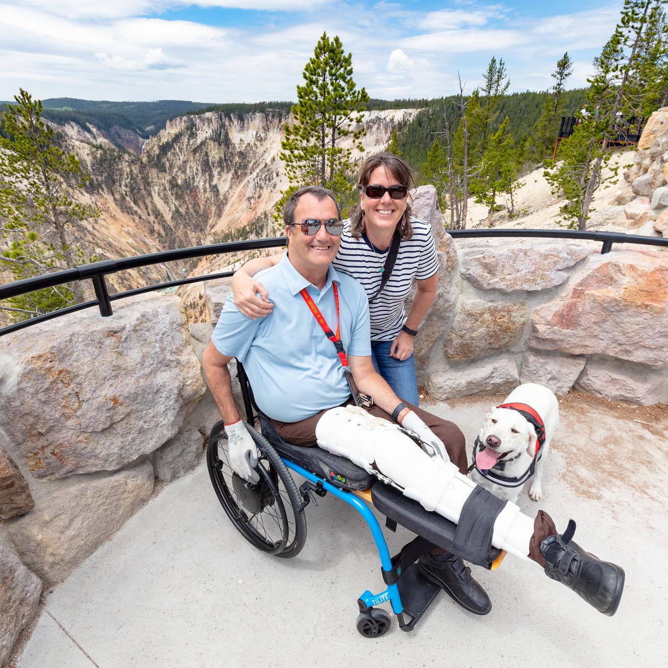Two people and a service dog take a photo near a canyon