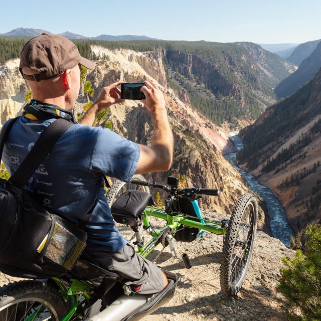 A person in a mobility chair photographs a canyon and river.