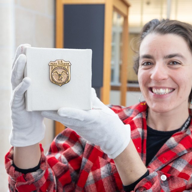 a woman smiling and holding up a National Park Service gold badge