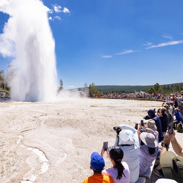 a crowd of people watching a geyser erupt