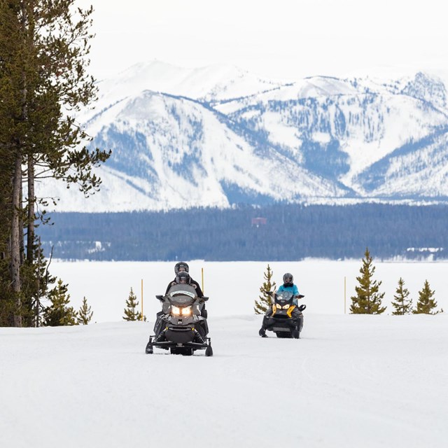 two snowmobilers driving on a snowy road