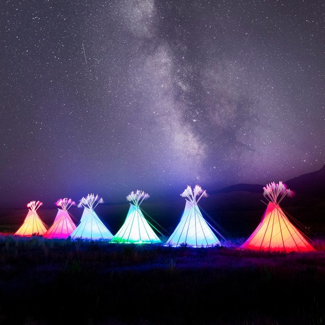 a row of illuminated, colorful teepees beneath a starry night sky
