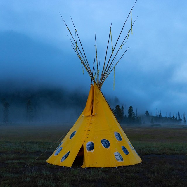 a large, yellow tipi structure in a valley on a foggy morning