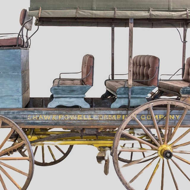 A painted Shaw and Powell Company wagon with a blue body, grey-green roof, yellow wheels.