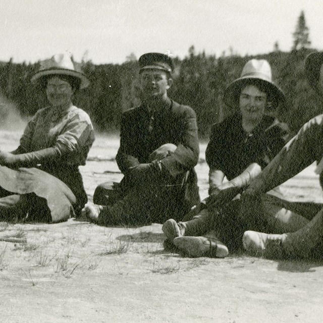 Three men and three women sitting on ground, smiling at camera