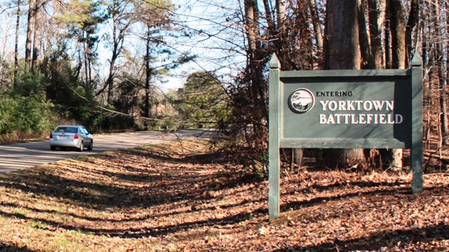 Car driving Colonial Parkway past sign that says, "Entering Yorktown Battlefield