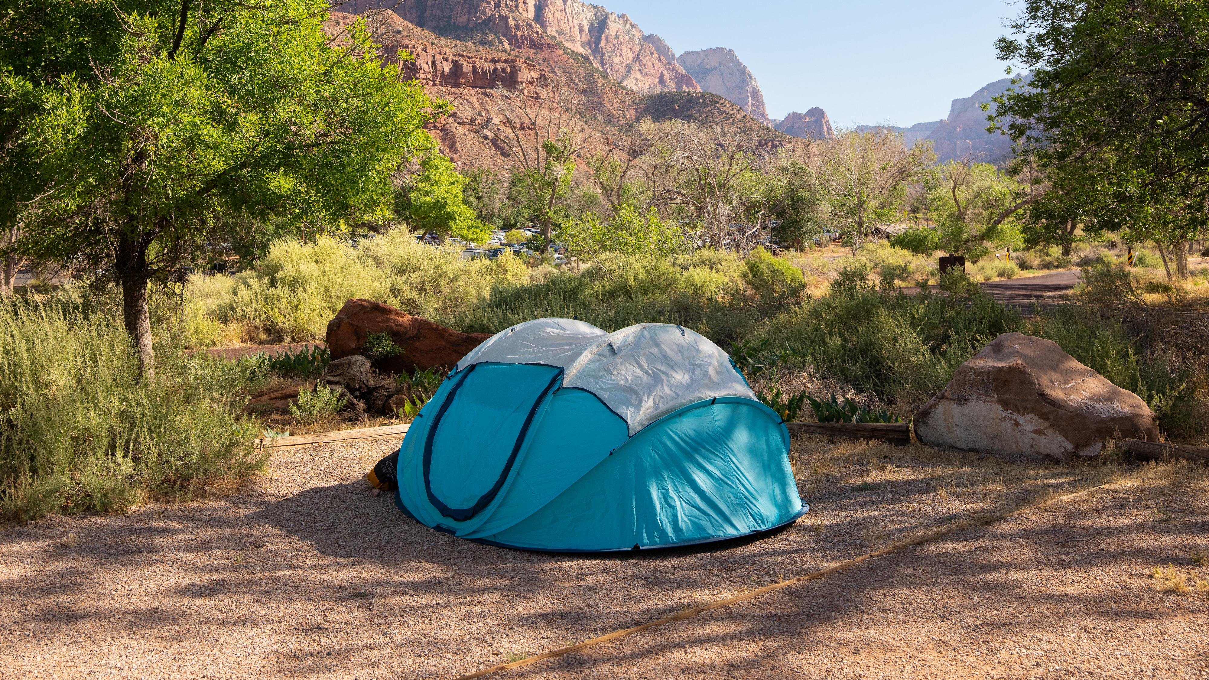 A tent in a gravel campsite. A large sandstone peak stands in the background.
