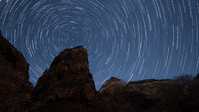 A long exposure image of Angels Landing with stars behind it