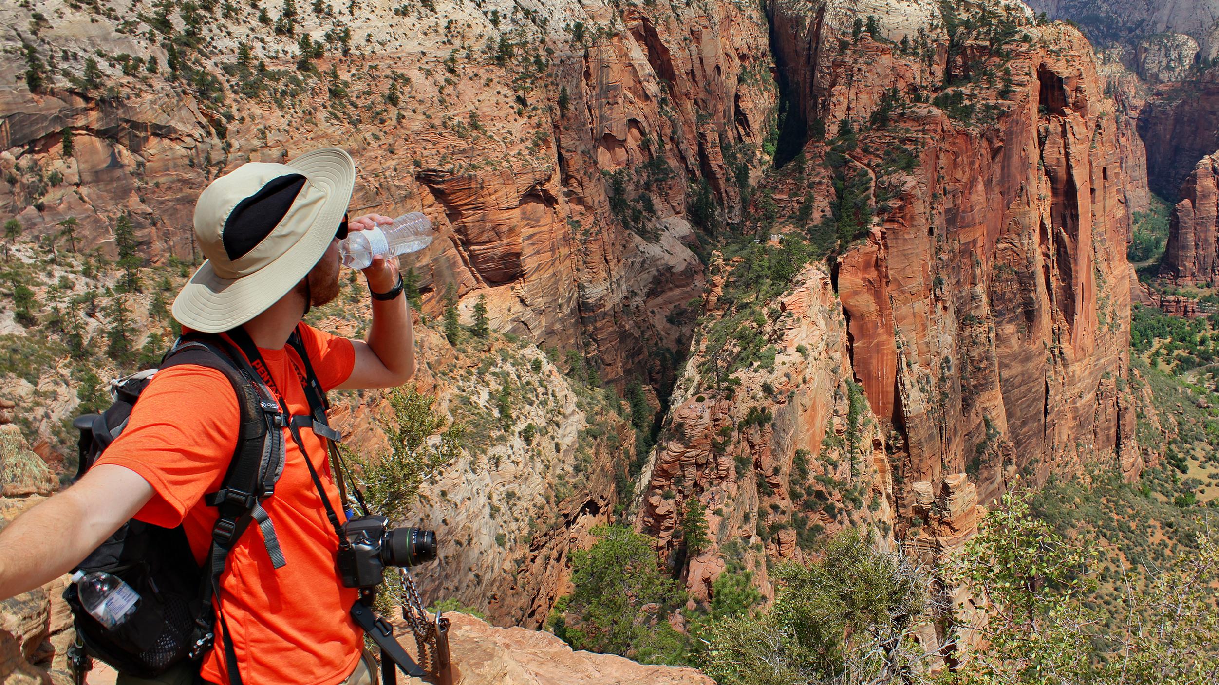 A hiker drinks water from a bottle as they gaze into Zion Canyon.