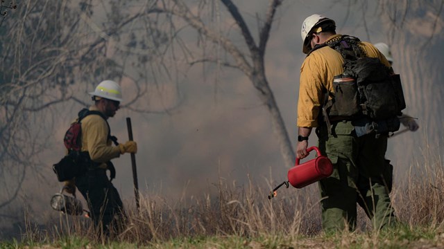 Two wildland fire crew members with burn torches. 