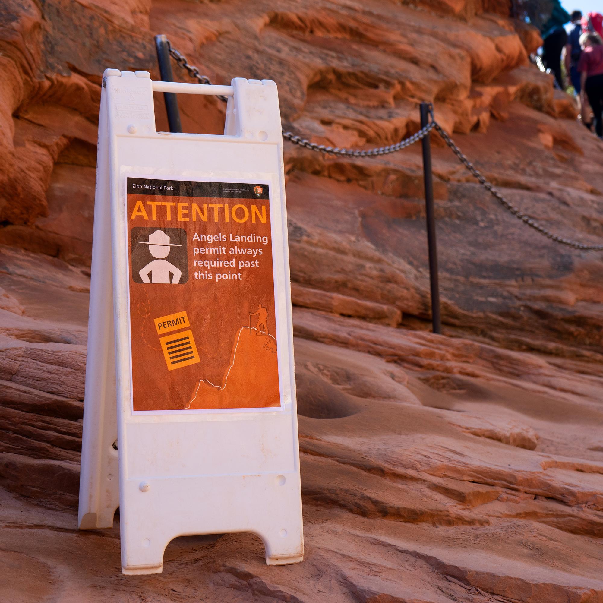 A sign on a white, plastic A-frame board stands next to the beginning of some steel chains.