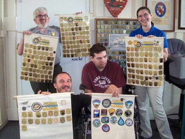 4 people holding up large cut fabric that is filled with Junior Ranger Badges from many NPS sites