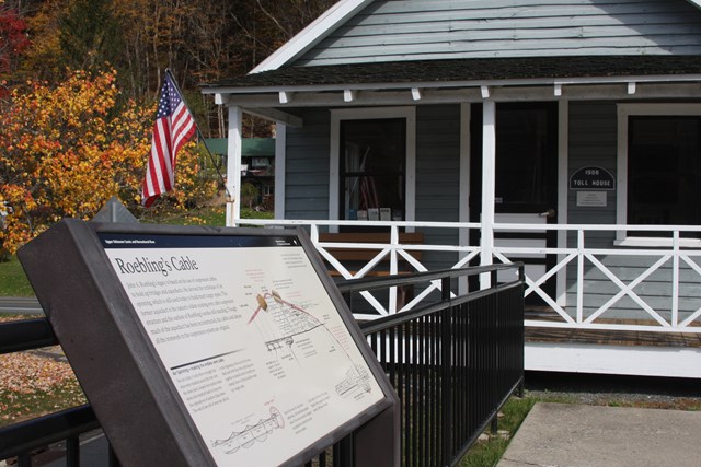 Blue building with covered porch and American flag. In foreground is wayside exhibit.