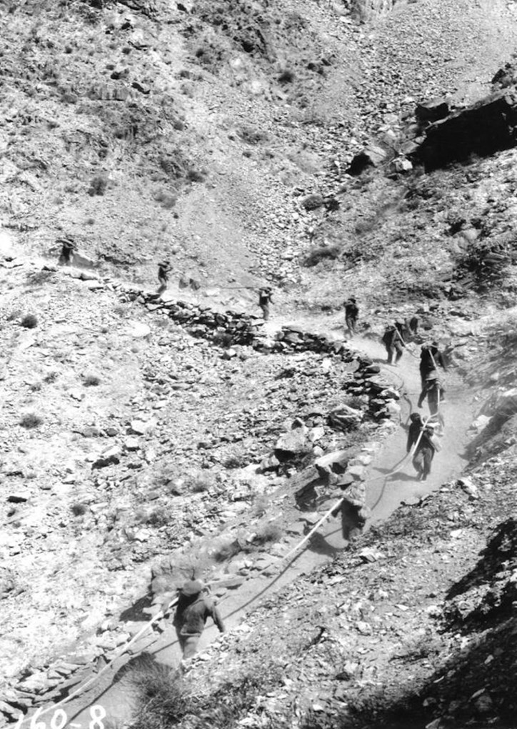Men carrying cable down rocky trail and cliffs