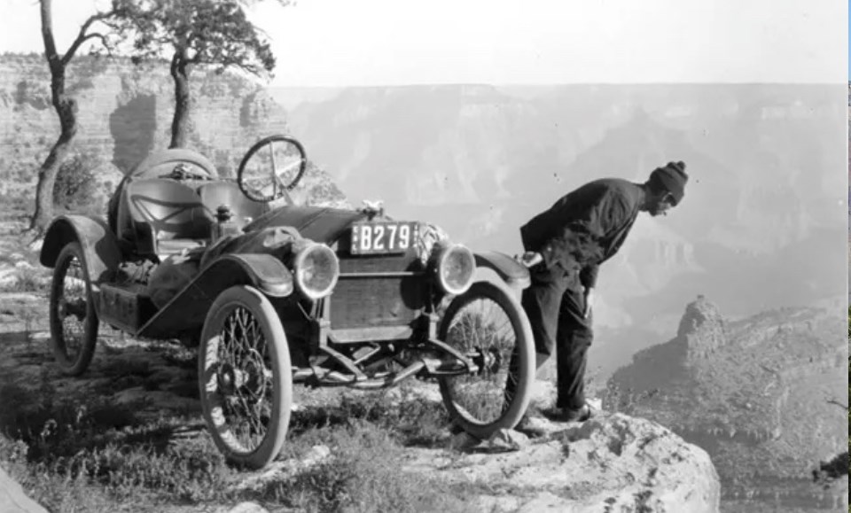 Old automobile on edge of cliff with man peering over edge