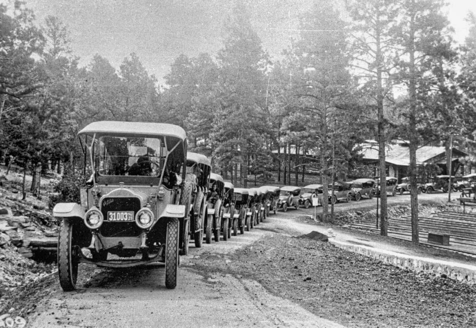 Line of old cars on road, building and trees in background