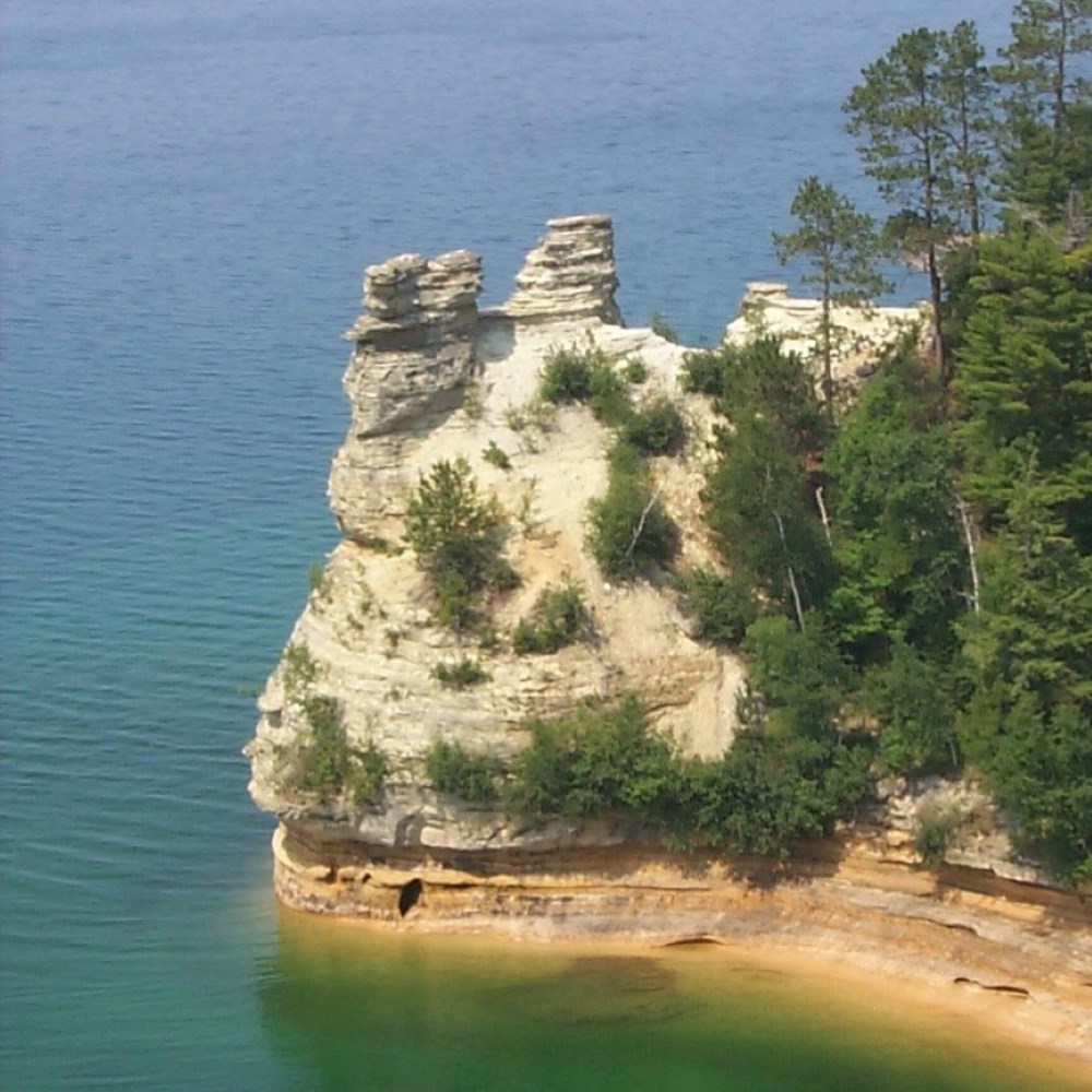 A sandstone rock formation with trees coming out of Lake Superior. The formation has two large formations on top (turrets).