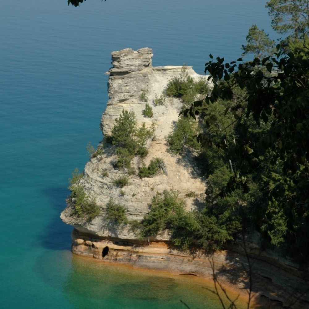 A sandstone rock formation with trees coming out of Lake Superior. The formation has two large formations on top (turrets).