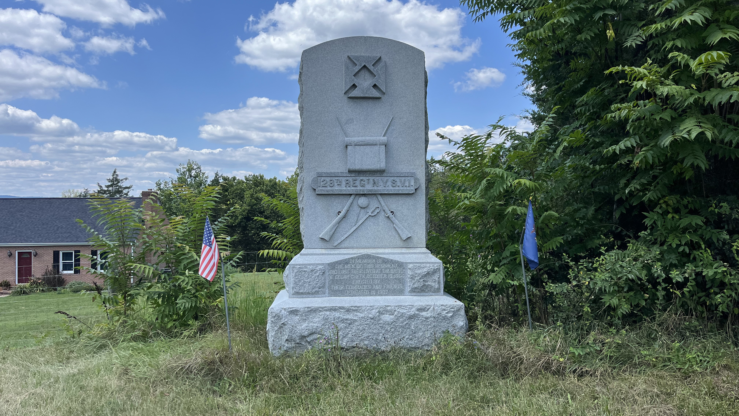 A tall stone monument displaying several military symbols including the Nineteenth Corps Badge, crossed rifles, a knapsack, and a sword. The inscription states,  "128th Regt N.Y.S.V.I."