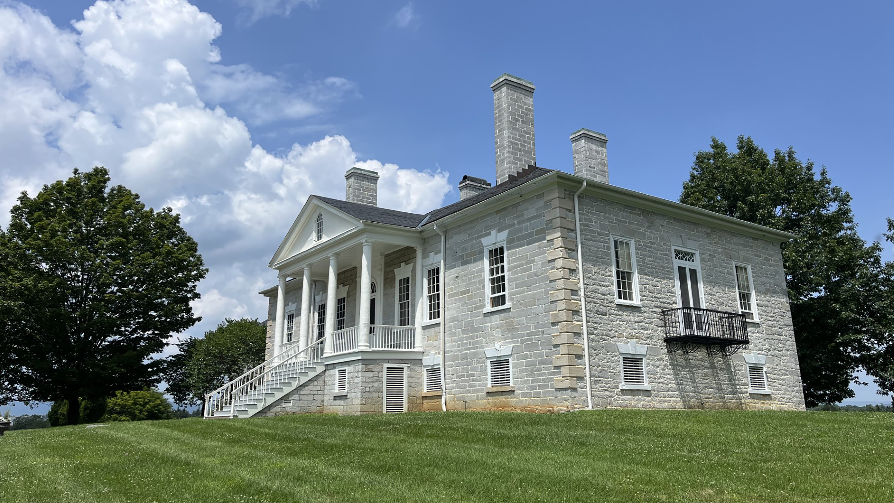 Large limestone plantation house, exterior stairs leading up to a columned front porch.