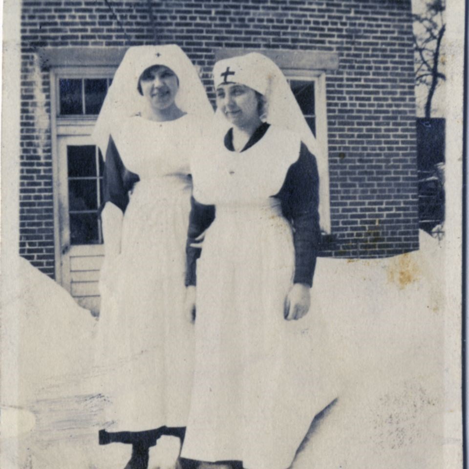 Standing in front of a probable hospital building, this pair of nurses pose for a picture.