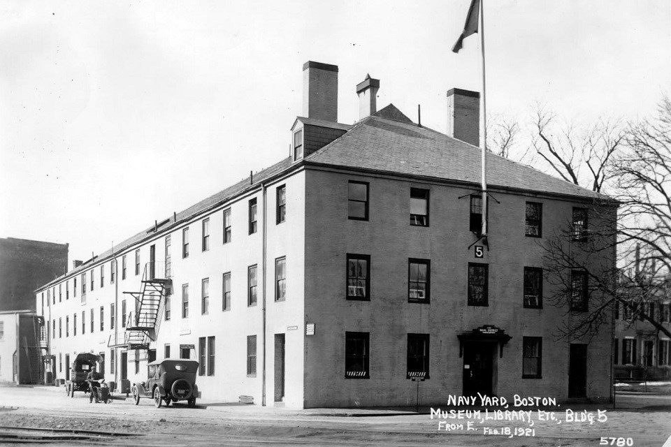 black and white photo of a brick building with a flagpole and two vintage cars