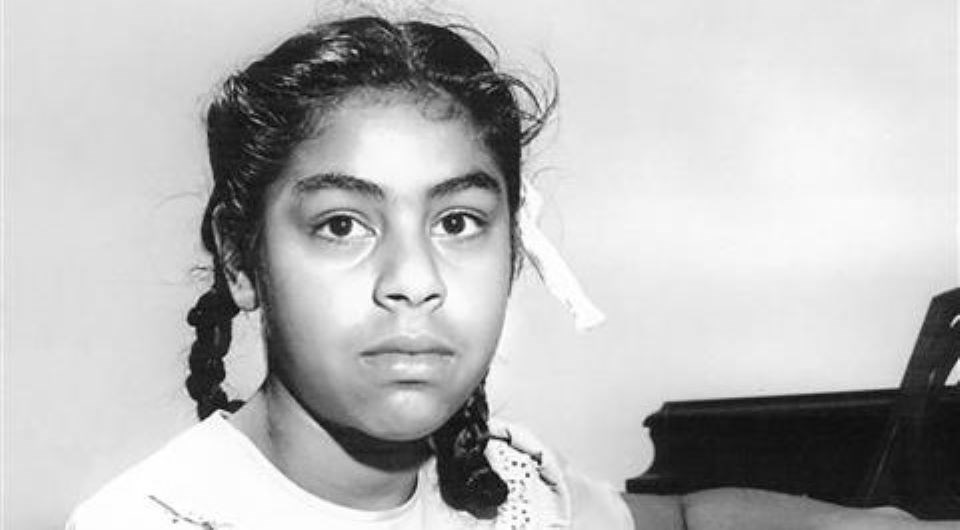 Black and white photo of a girl with braided pigtails showing her face and shoulders.