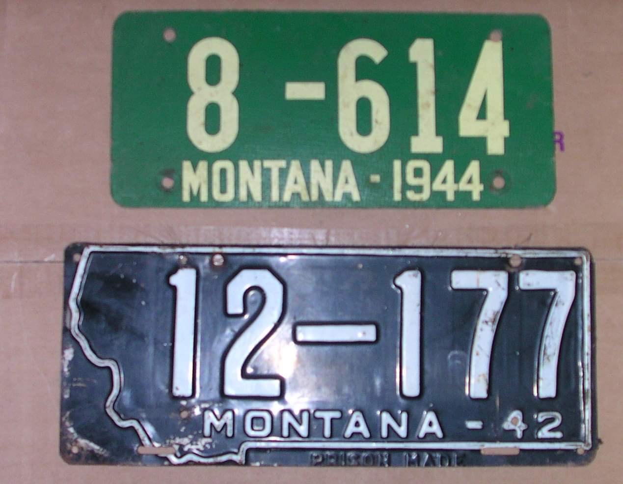 A green license plate with numbers and Montana 1944 over a black license plate with the shape of Montana and labeled Montana-42