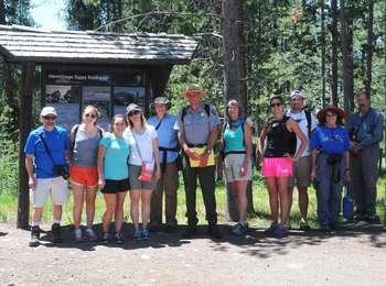 Ranger with group of hikers at the Hermitage Point Trailhead partly shaded by lodgepole pines.