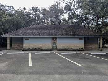 Additional parking and restrooms are located along the entrance road loop, on the out-bound side.  The single story restroom building is tan stone block with gray, planked wood siding on the upper half of the walls. As you face the building from the parking lot, signage shows that accessible restrooms for men are on the left side of the building and, for women, on the right.  The side of the building facing the parking lot has one foot high plant beds that stick out by about one foot. In the center of that wall is a water fountain, with a water bottle re-filling station. Mounted above the fountain is a National Park Service logo, described later.  On the right, or west, side of the building is a large bulletin board, flanked by vending machines. To the right of the building is the entrance to a nature trail.  The National Park Service logo is a brown arrowhead, pointed downward. Inside the arrowhead are the words in white lettering, â€œNational Park Serviceâ€, with a green sequoia tree shape to its left. Near the bottom of the arrowhead is a white buffalo silhouette set against a green meadow, with a white lake and snowcapped mountain behind it. 