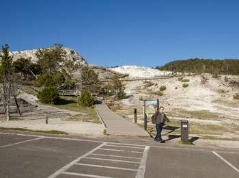 A man walks away from a boardwalk that descends from travertine terraces