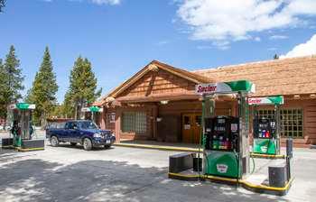 Four gas pump stations in front of a one-story building with covered entrance and wood shingled-roof