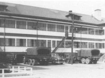 Army vehicles are parked outside the two story barracks in this black and white photograph