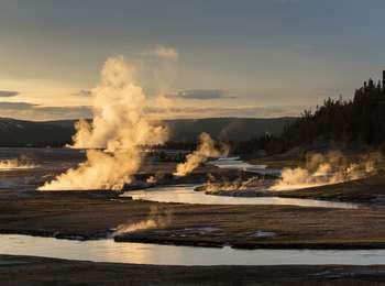 Steam illuminated by sunset rises above a winding river