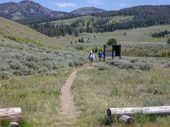 A pair of hikers finishing their hike by passing the trailhead information sign.