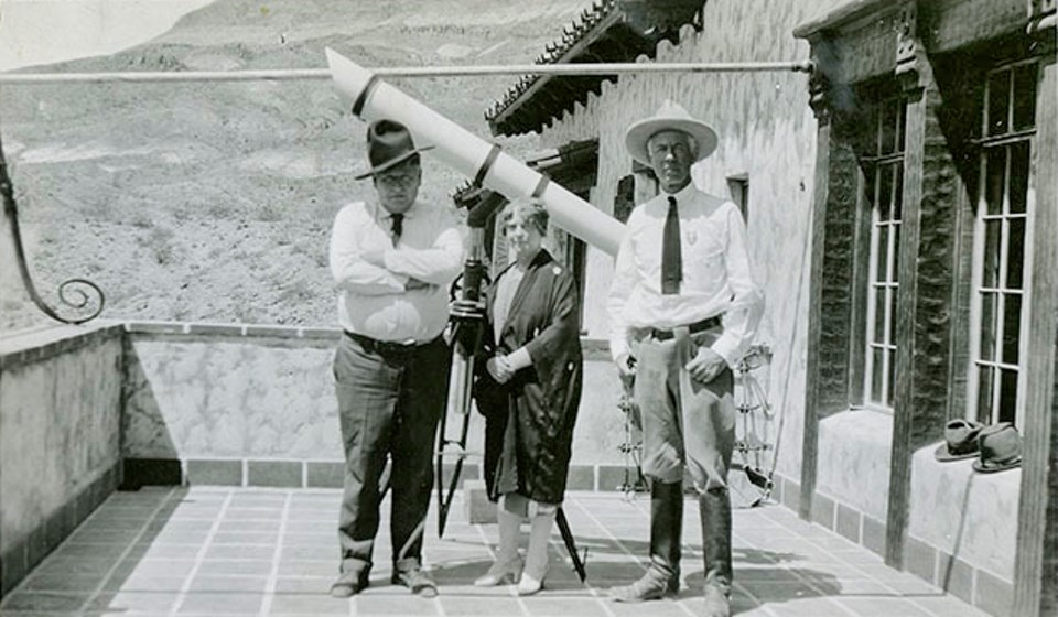 Two men and a woman on a porch next to a telescope.