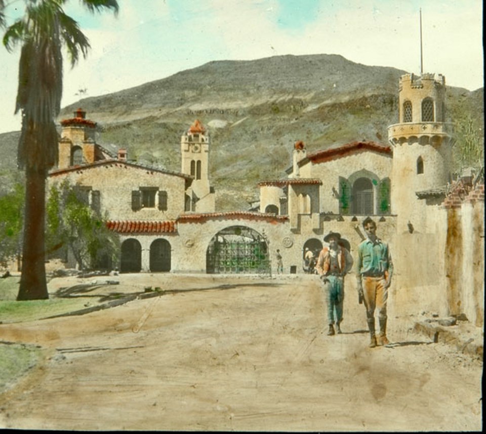 Man and woman walking with Spanish-style buildings behind them.