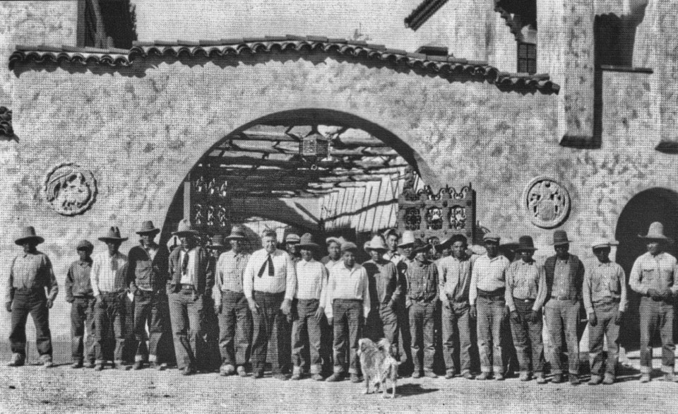 A group of men stand in front of arched entrance to buildings.