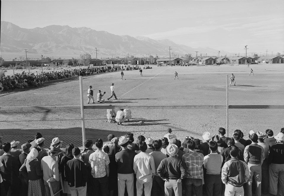 Spectators watch a baseball game with mountains in background.