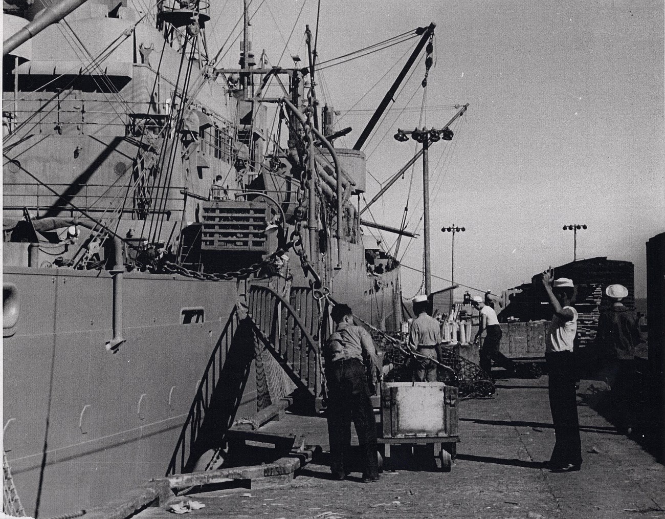 Four African American sailors are seen loading munitions onto a large ship.