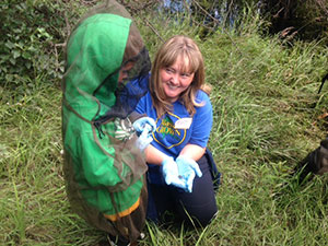 A woman holding a wood frog holds it up for a boy in a mosquito net to see