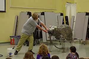 A man shows students how a trash-art-bear sculpture was created