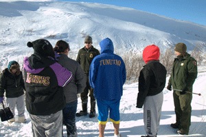 Students gather around park rangers while backdropped by a snowy mountain