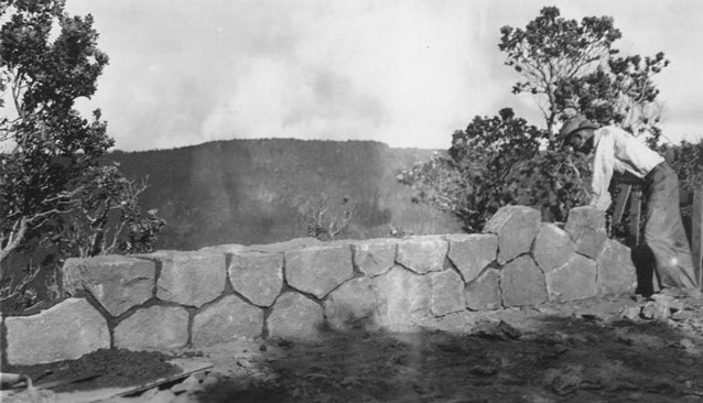 A man leans to look over a carefully-laid, mortared stone guard wall.