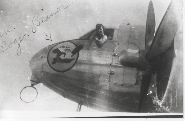 A man hangs out of the cockpit of a prop plane with a beaver insignia on the nose