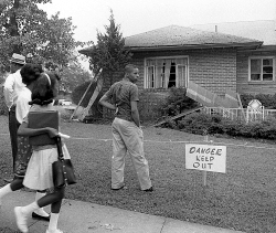 Man stands in front of house with 'Danger Keep Out' sign; B&W photo