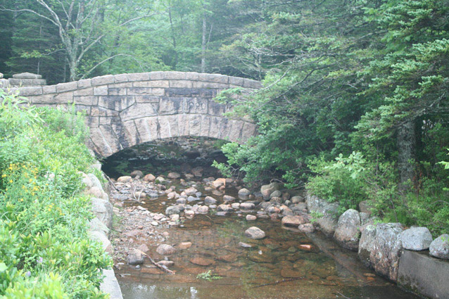 A stone bridge arches over a shallow, stone-lined stream. (OCLP, 2008)