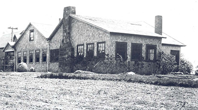 Windows surround the perimeter of a low, rambling house in a black and white image.